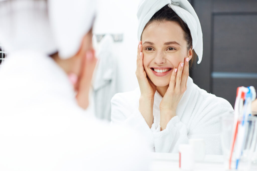Woman viewing skin in the mirror after receiving VAMP Advanced Microneedling treatment.